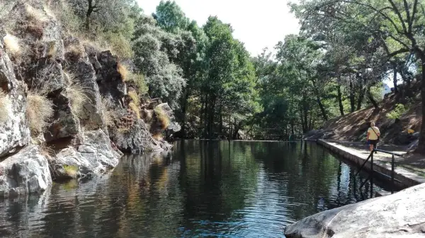 Un hombre camina por el borde de piscinas naturales cerca de la alberca, rodeadas de rocas y vegetación frondosa.