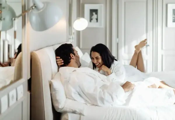 Ett lyckligt par i morgonrockar skrattar i en lyxig säng, kanske på ett hotell i St. Gallen.