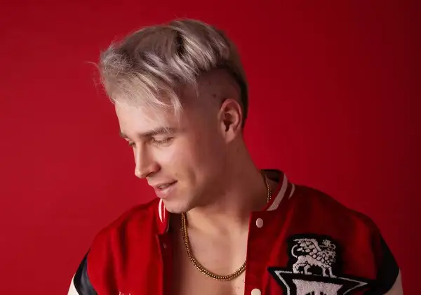 Młody mężczyzna z blond włosami i złotym łańcuchem na szyi, w czerwonej kurtce. Ile lat ma Skolim?