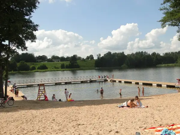 Letnie popołudnie na piaszczystej plaży nad jeziorem. Ludzie odpoczywają, kąpią się, a dzieci bawią się w wodzie. To typowy widok dla mazurskich miejscowości.