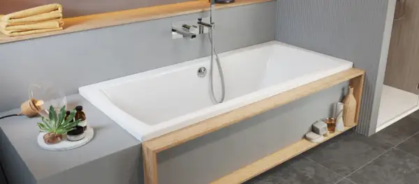 Moderne Badewanne einbauen: Weiße Wanne mit Holzakzenten, Armatur und Handbrause. Dekorative Elemente wie Lampen und Flaschen schmücken die Ablage.