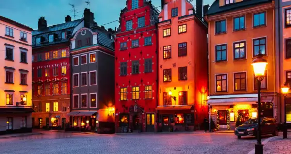 Färgstarka hus i **altstadt Stockholm** lyser upp en kullerstensbelagd gata i skymningen.
