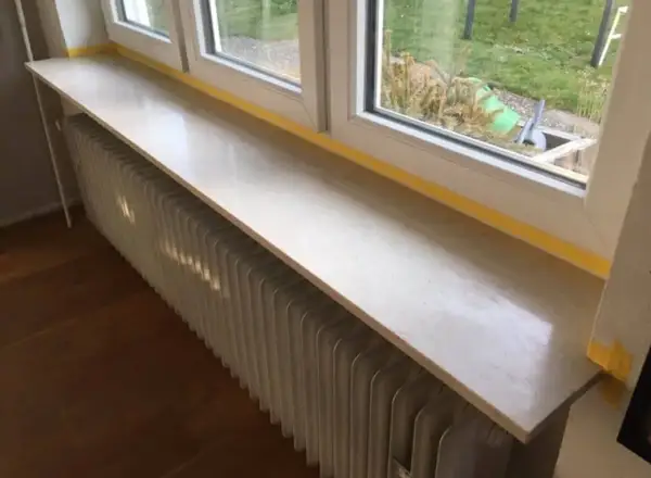 Un nouveau rebord de fenêtre en pierre, prêt à accueillir des plantes, surplombe un radiateur blanc.