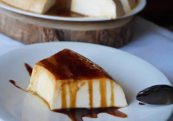 Un trozo de tarta de cuajada, cubierto de caramelo líquido, reposa en un plato blanco.