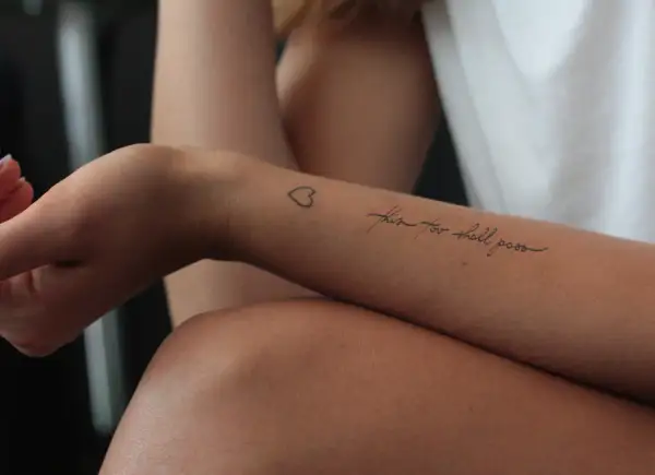Ein Tattoo auf dem Unterarm einer Frau mit der Aufschrift "this too shall pass" und einem kleinen Herz. Ein Symbol der Hoffnung nach der Überwindung von Alkoholsucht.