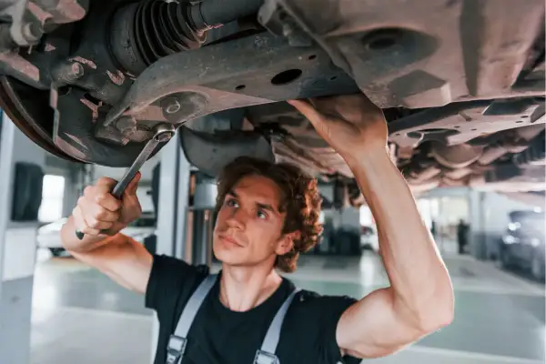 Mechanik naprawia zawieszenie auta, podejrzewając jazdę z uszkodzoną tuleją wahacza.