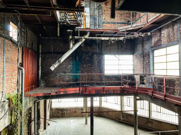 Intérieur d'une usine abandonnée, typique d'un site d'urbex dans la Somme. Structures métalliques rouillées, tuyaux, briques apparentes et lumière filtrant par les fenêtres.