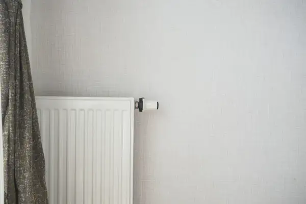 Radiateur blanc moderne, prêt à être alimenté par une pompe à chaleur. Un rideau discret complète la scène.