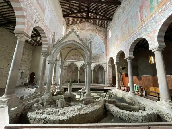 Interno della Basilica di San Piero a Grado, con affreschi medievali e resti archeologici al centro.