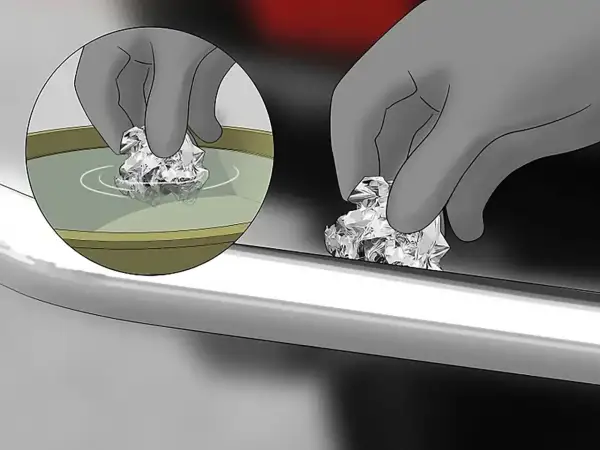 Mano con guanto pulisce con carta stagnola una cromatura rovinata, immergendola prima in un liquido.