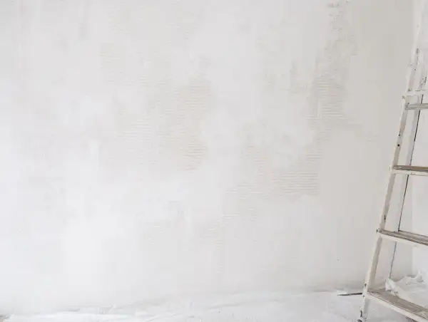 Étape de nettoyage d'un mur blanc jauni, une échelle est visible sur la droite.