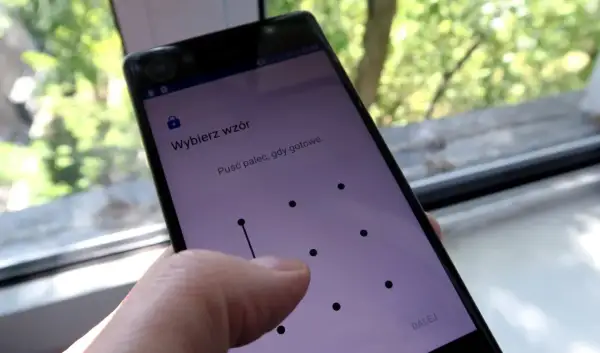 Telefon z ekranem blokady, gdzie wybierasz **wzór** 15 najpopularniejszych blokad. Palec rysuje linię na siatce kropek.