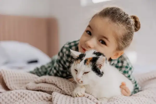 Mała dziewczynka przytula swojego kota. Ich więź jest widoczna, gdy kot wtula się w jej ramiona.