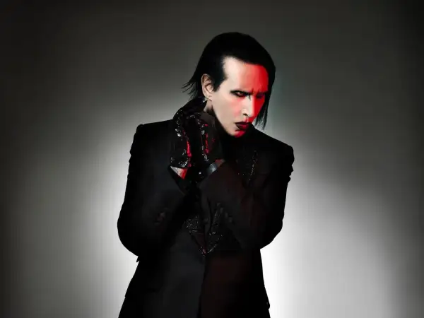 Marilyn Manson zespół w czarnym garniturze, z czerwonym makijażem i rękawiczkami.