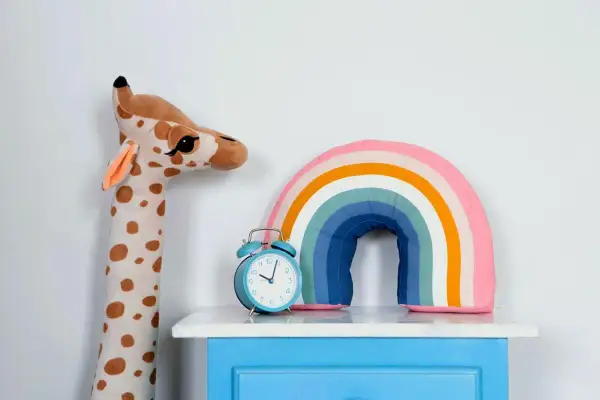 Plüsch-Giraffe, Regenbogen-Kissen und Wecker auf blauem Nachttisch – süße kinderzimmer deko diy.