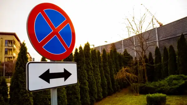Znak zakazu zatrzymywania się i postoju, z tabliczką wskazującą kierunki. Uważaj, bo grozi za to mandat.