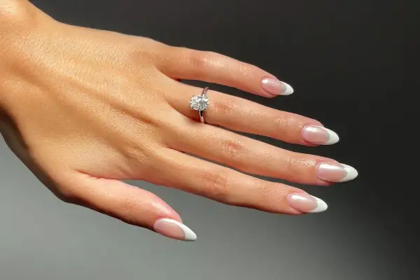 Dłoń z pierścionkiem zaręczynowym i idealnymi paznokciami na zaręczyny. Klasyczny french manicure podkreśla blask kamienia.