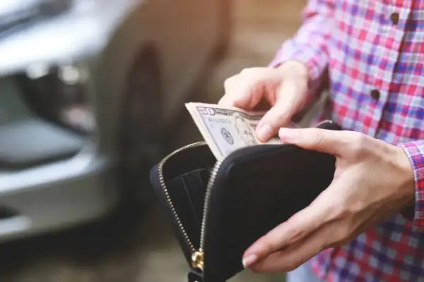 Ręce wyciągają banknot 50 dolarów z portfela, przygotowując się do kupna samochodu od osoby prywatnej.