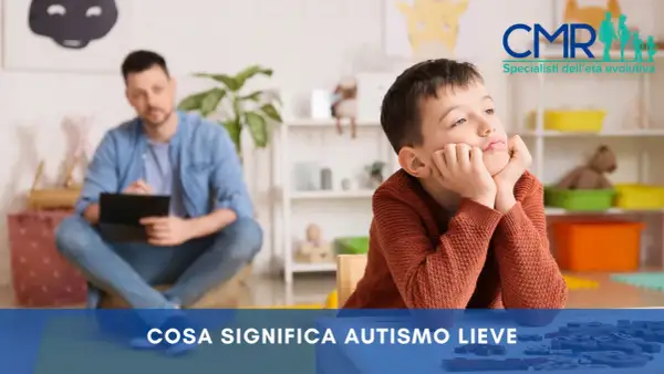 Bambino pensieroso in terapia, con un uomo sullo sfondo. Si parla di autismo lieve e della sua percentuale di invalidità.
