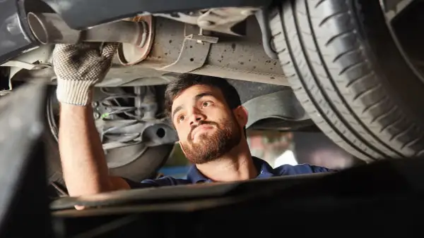 Mechanik w rękawiczce sprawdza podwozie samochodu, wykonując naprawę układu wydechowego.