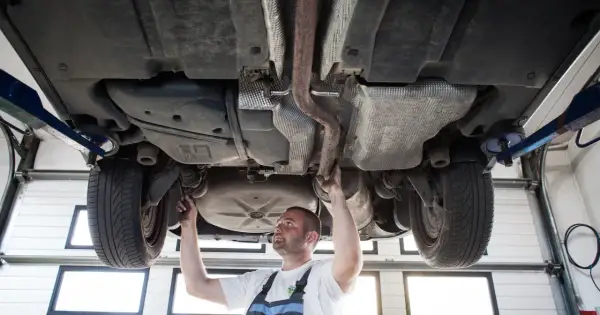 Mechanik sprawdza podwozie sedana na podnośniku, badając układ wydechowy i zawieszenie.