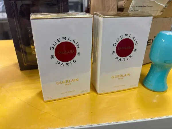 Dwie białe perfumy Samsara Guerlain 75 ml, każda w złotym opakowaniu, stoją na żółtej powierzchni.