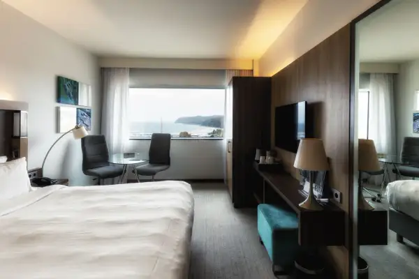 Pokój w hotelu Marriott Gdynia z widokiem na morze. Wygodne łóżko, stolik z krzesłami i telewizor.