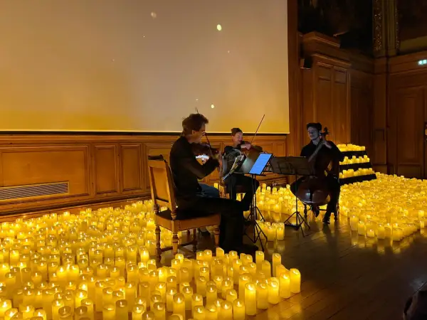 Un trio de musiciens joue dans une salle baignée par la douce lueur de milliers de bougies. Un concert à la bougie magique.