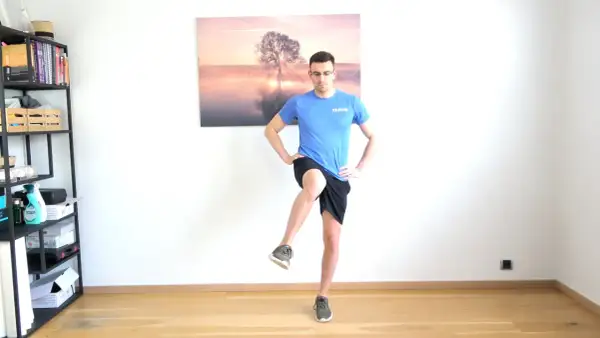 Homme effectuant un exercice de rotation interne hanche, jambe levée, mains sur les hanches.