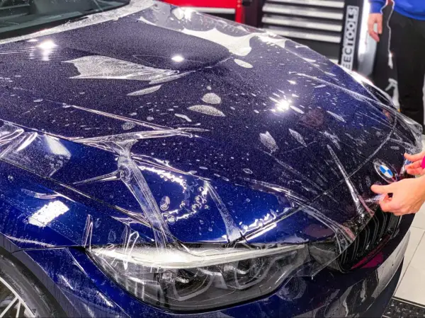 Niebieski **car color** z folią ochronną na masce. Widać krople wody i pęcherzyki powietrza pod folią.