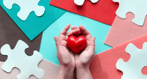 Mani che stringono un cuore rosso, circondate da pezzi di puzzle bianchi e sfondi colorati. Un gesto d'amore, perché si può fare una donazione tra fratelli.