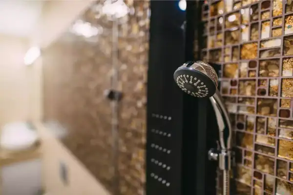 Une colonne de douche moderne avec un pommeau chromé et des jets intégrés, prête à installer dans une salle de bain aux murs mosaïqués.