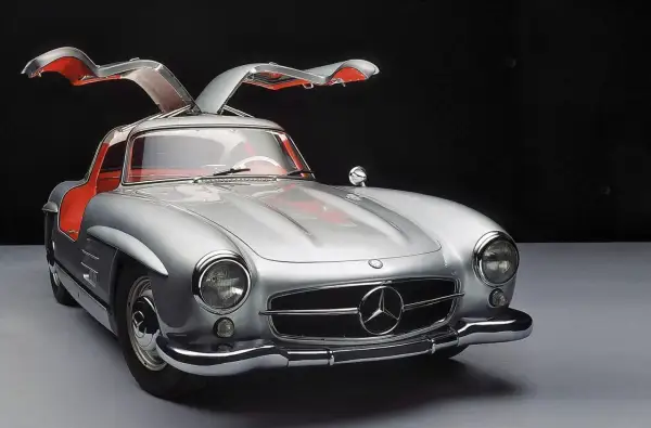 Srebrny Mercedes 300SL z otwieranymi do góry drzwiami, z czerwonym wnętrzem, prezentuje się elegancko na ciemnym tle.