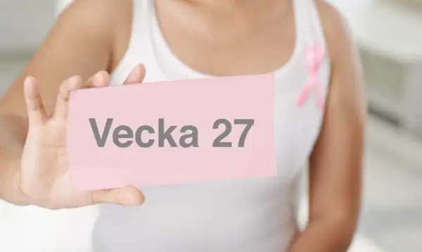 Gravid vecka 27. En person håller upp en rosa lapp med texten "Vecka 27". En rosa band pryder personens vita linne.