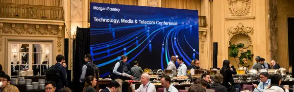 Attendees mingle at a Morgan Stanley TMT conference, with a large screen displaying the event title and a blue, abstract network graphic.