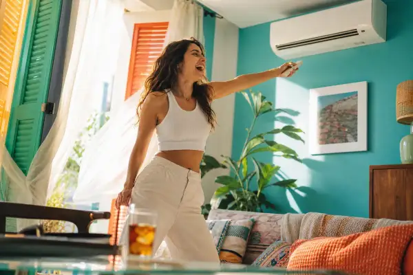 Femme joyeuse ajustant le **dehum climatiseur** avec une télécommande, profitant de la fraîcheur dans un salon lumineux.