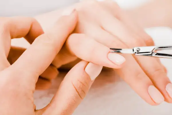 Unghie curate: una mano assiste l'altra con forbicine per unghie, mostrando come si fanno le unghie perfette.