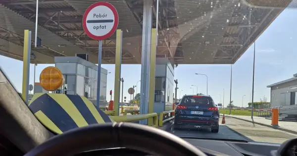 Kolejka samochodów na autostradzie A4 przed punktem poboru opłat. Widać bramki, znaki drogowe i samochody czekające na przejazd.