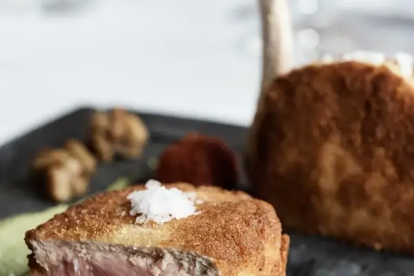Ein knuspriges Kalbsschnitzel, italienisch zubereitet, mit feinen Beilagen auf einem dunklen Teller.