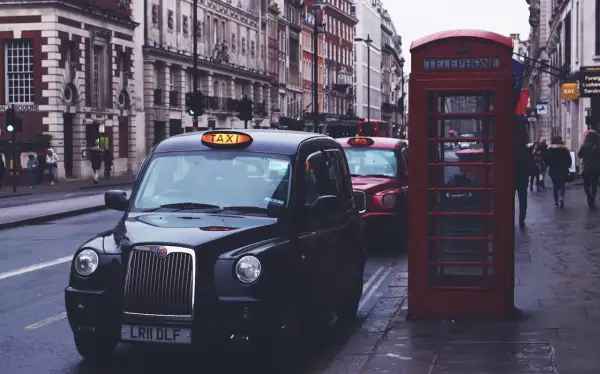 Czarne taksówki i czerwona budka telefoniczna na ulicy w Londynie.
