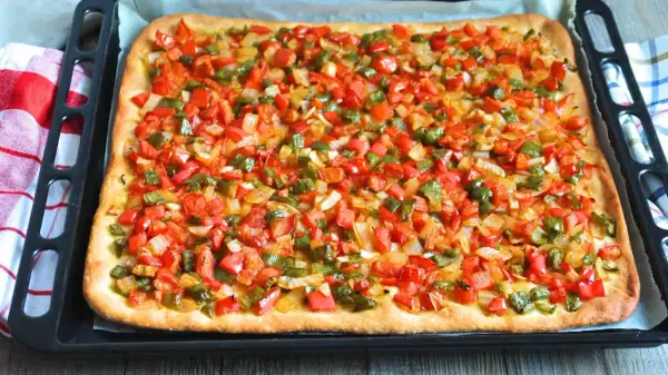 Coca mallorquina recién horneada, cubierta con pimientos rojos y verdes picados y cebolla.