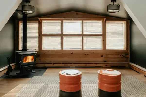 Une cheminée dans une véranda confortable, avec des flammes vives réchauffant la pièce. Deux poufs orange vif invitent à la détente.