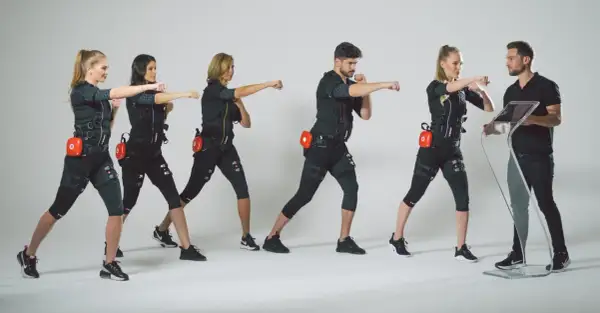 Grupa osób w strojach EMS ćwiczy pod okiem trenera. Dowiedz się, ile kosztuje trening EMS i zacznij swoją metamorfozę!