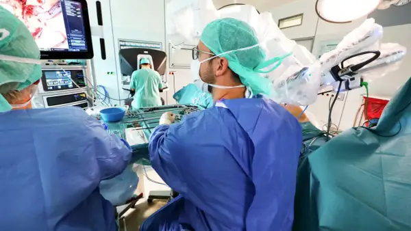 Chirurgen im OP-Saal bereiten sich auf eine onkologische Chirurgie vor, mit Fokus auf einem Monitor, der das Operationsfeld zeigt.