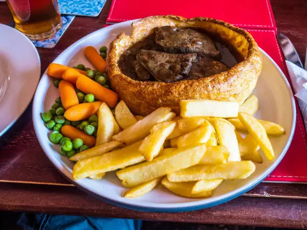 Pyszne danie kuchni brytyjskiej: pieczeń wołowa w Yorkshire puddingu, podana z frytkami, groszkiem i marchewką.