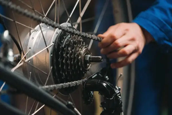 Ręka reguluje przerzutki w rowerze, poprawiając płynność jazdy. Widoczna kaseta Shimano i przerzutka.