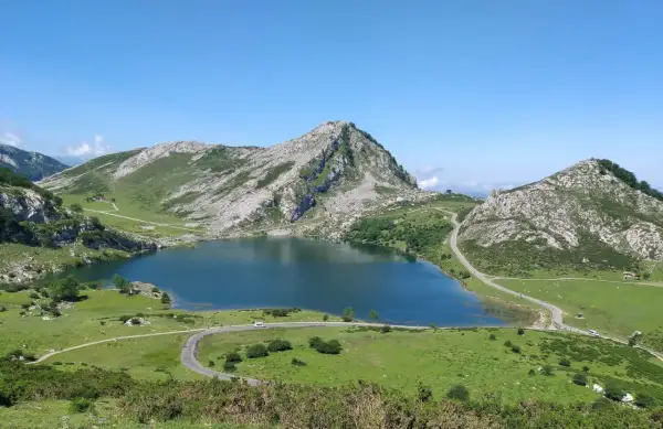 Lago Ercina en la montaña de Covadonga, rodeado de verdes prados y picos rocosos bajo un cielo azul.