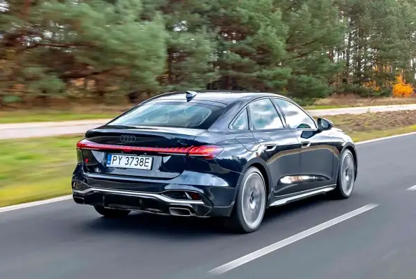 Ciemny Audi A4 B10 w wersji sedan pędzi po drodze, otoczony jesiennym lasem.
