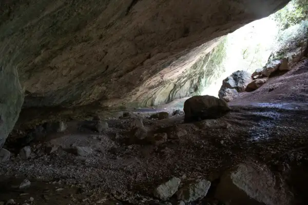 L'interno di una grotta con rocce sparse e un'apertura luminosa che rivela la valle scappuccia.