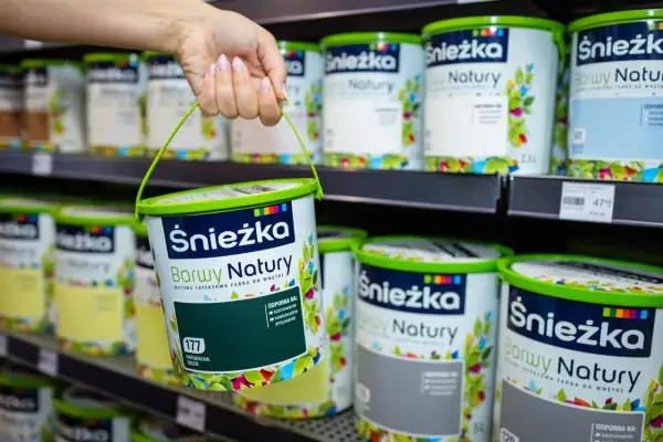 Ręka trzyma wiaderko z zieloną farbą Śnieżka Barwy Natury. Na półce widać wiele innych puszek tych farb.